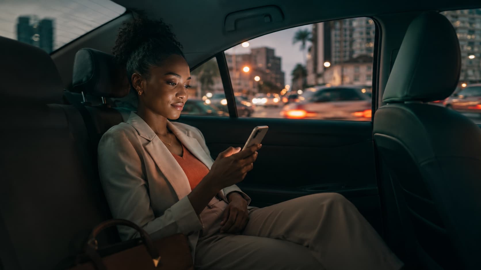 Rider relaxing in the back seat at dusk, choosing an offer on her phone